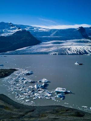 A glacial lagoon with icebergs, a glacier, mountains, and a small boat.
