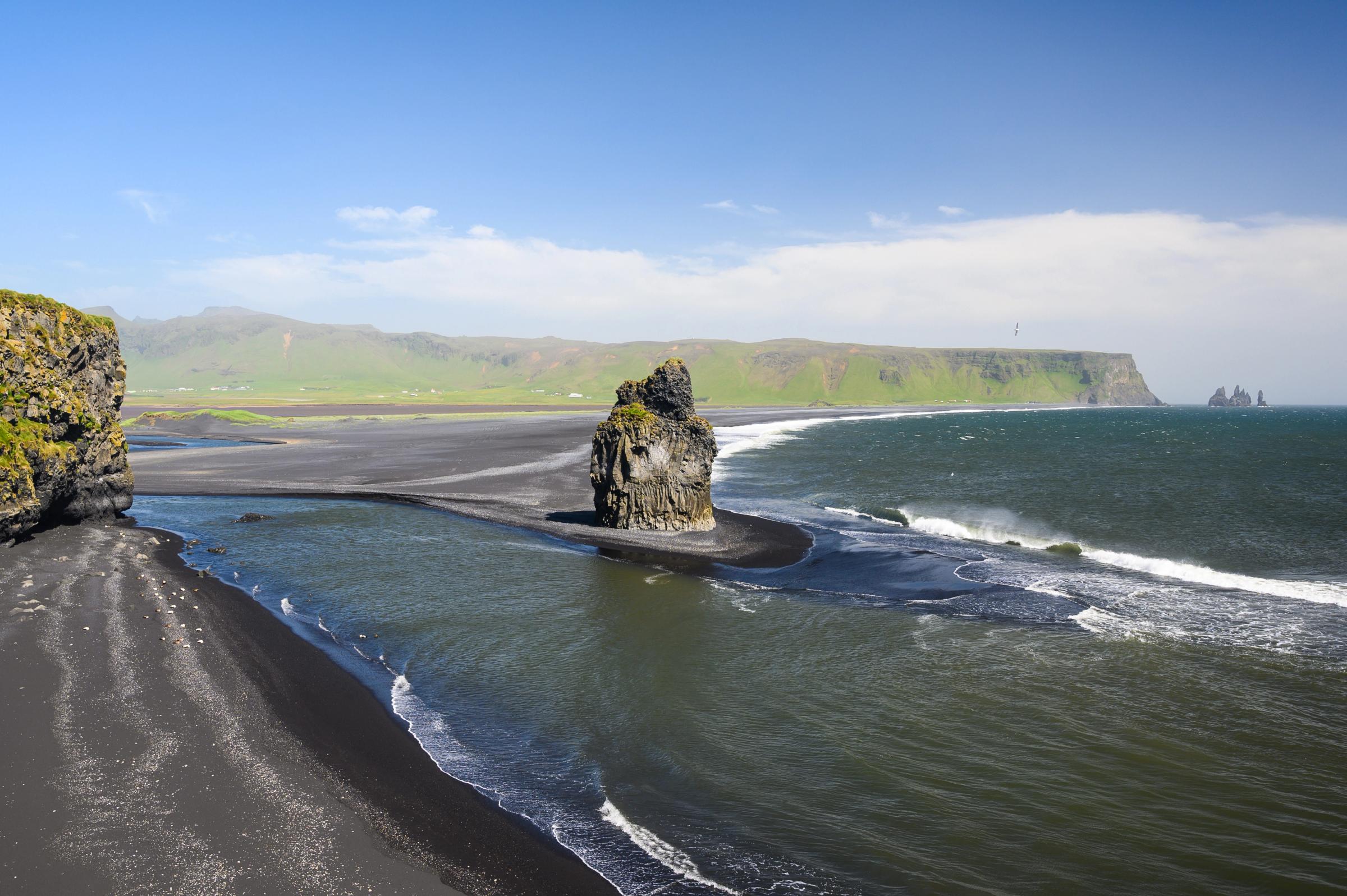 a black sand beach with a big rock in the middle on a sunny day