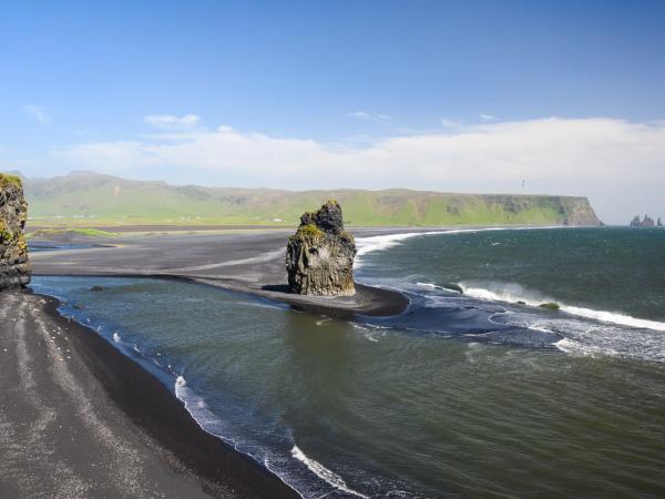 a black sand beach with a big rock in the middle on a sunny day