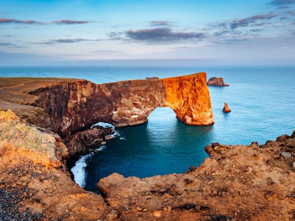 A large natural rock arch extending from a cliff into the ocean under warm light.