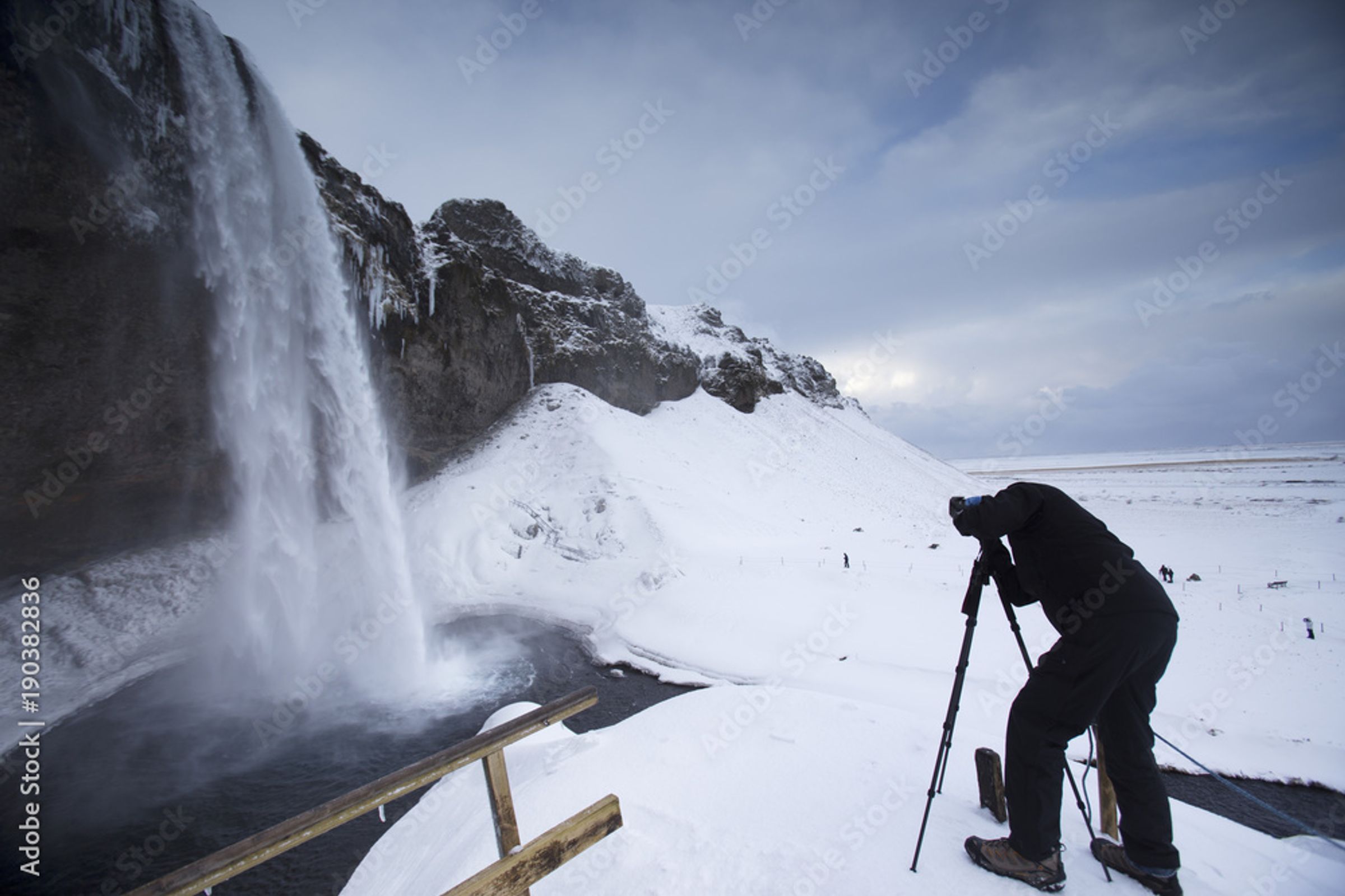a man taking a photo of a waterfall during winter