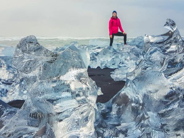 Chica vestida de rojo en una playa de arena negra llena de pequeños iceberes