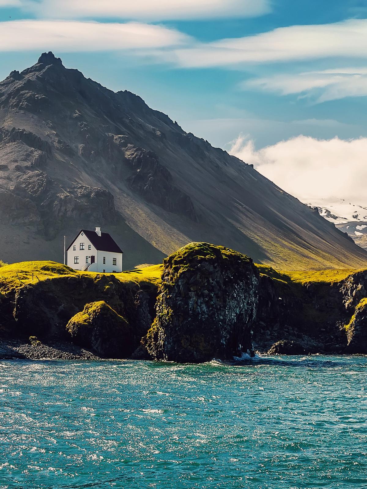 a small white house is sitting on top of a rocky hill next to the ocean .