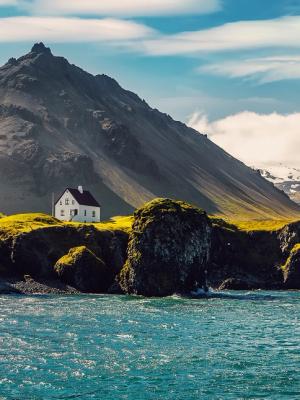 una pequeña casa blanca está situada en la cima de una colina rocosa junto al océano.