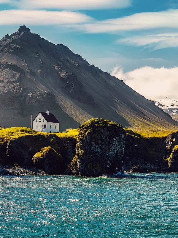 a small white house is sitting on top of a rocky hill next to the ocean .