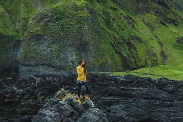 a woman in a yellow jacket and hiking boots on top of a rock