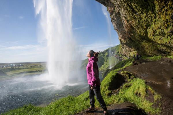 a woman in a purple jacket is standing in front of a waterfall.