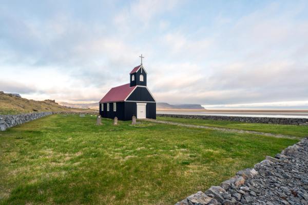 a small black church with a red roof is sitting in the middle of a grassy field .
