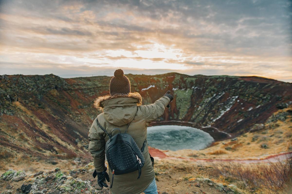 a woman is standing on top of a mountain pointing at a lake at Kerið in south iceland.