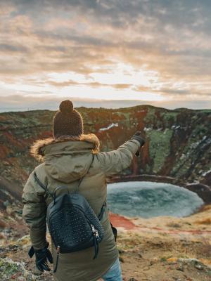 a woman is standing on top of a mountain pointing at a lake at Kerið in south iceland.