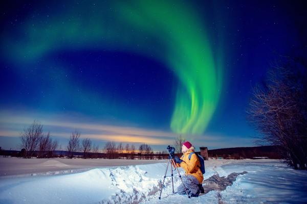 a person is kneeling in the snow taking a picture of the aurora borealis .