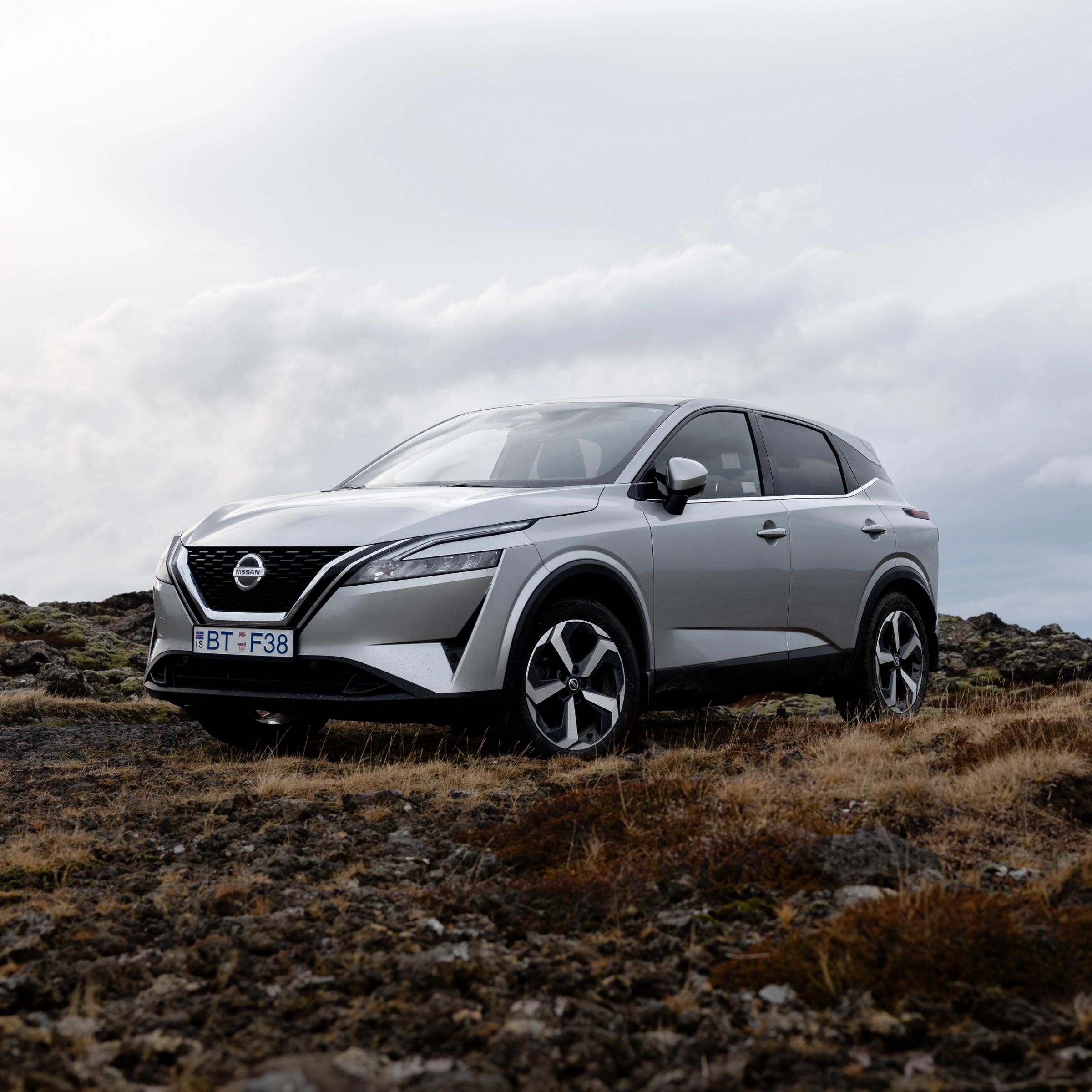 A silver Nissan Qashqai SUV parked on a rugged, rocky landscape under an overcast sky.