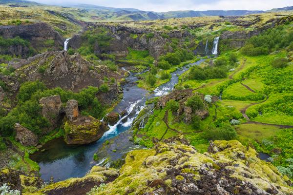 A lush green canyon with a river, two waterfalls, and winding paths.