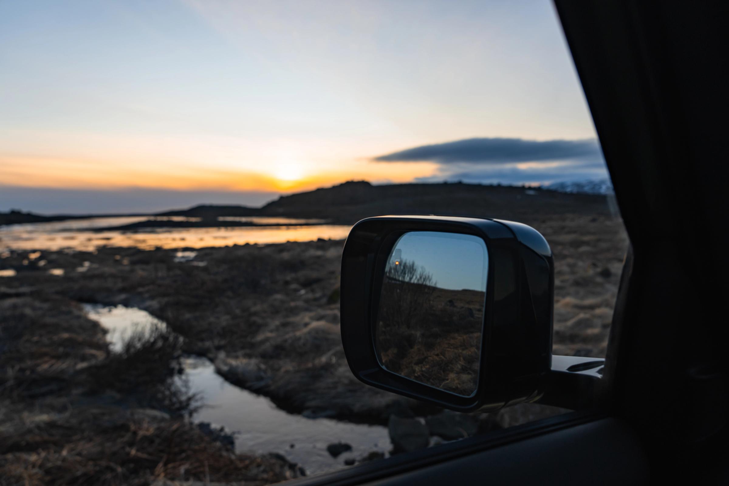 Atardecer islandés sobre los humedales, reflejado en el retrovisor lateral de un Land Rover Defender de alquiler de Go Car Rental