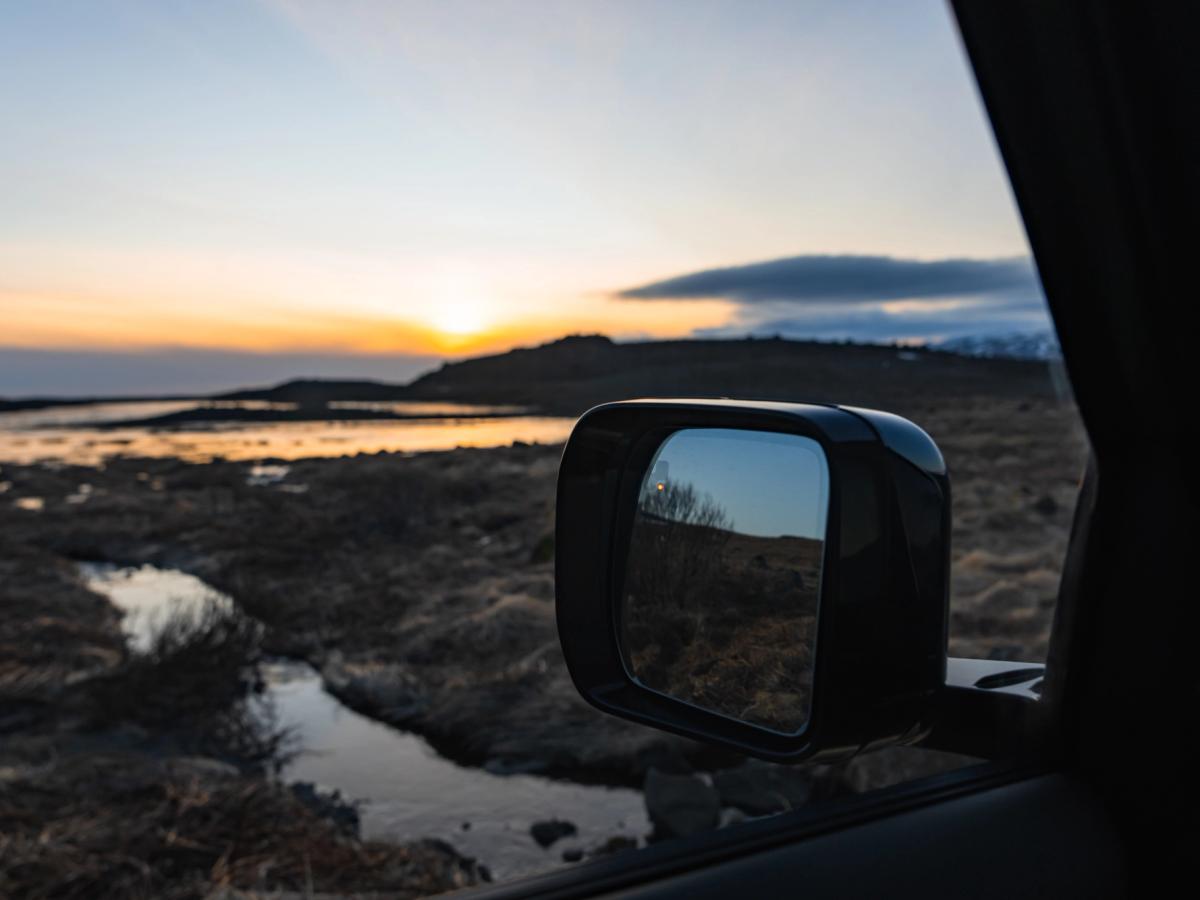 Atardecer reflejado en el retrovisor lateral del Land Rover Defender Atardecer islandés sobre los humedales, reflejado en el retrovisor lateral de un Land Rover Defender de alquiler de Go Car Rental