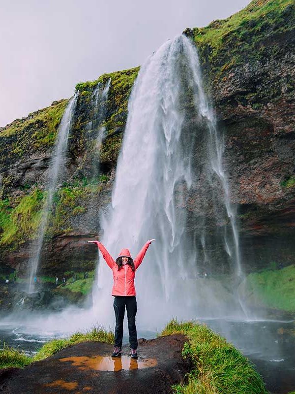 Best Things to do in Iceland Woman in front of one of the waterfalls of Iceland, happy to discover the country and its sumptuous landscapes