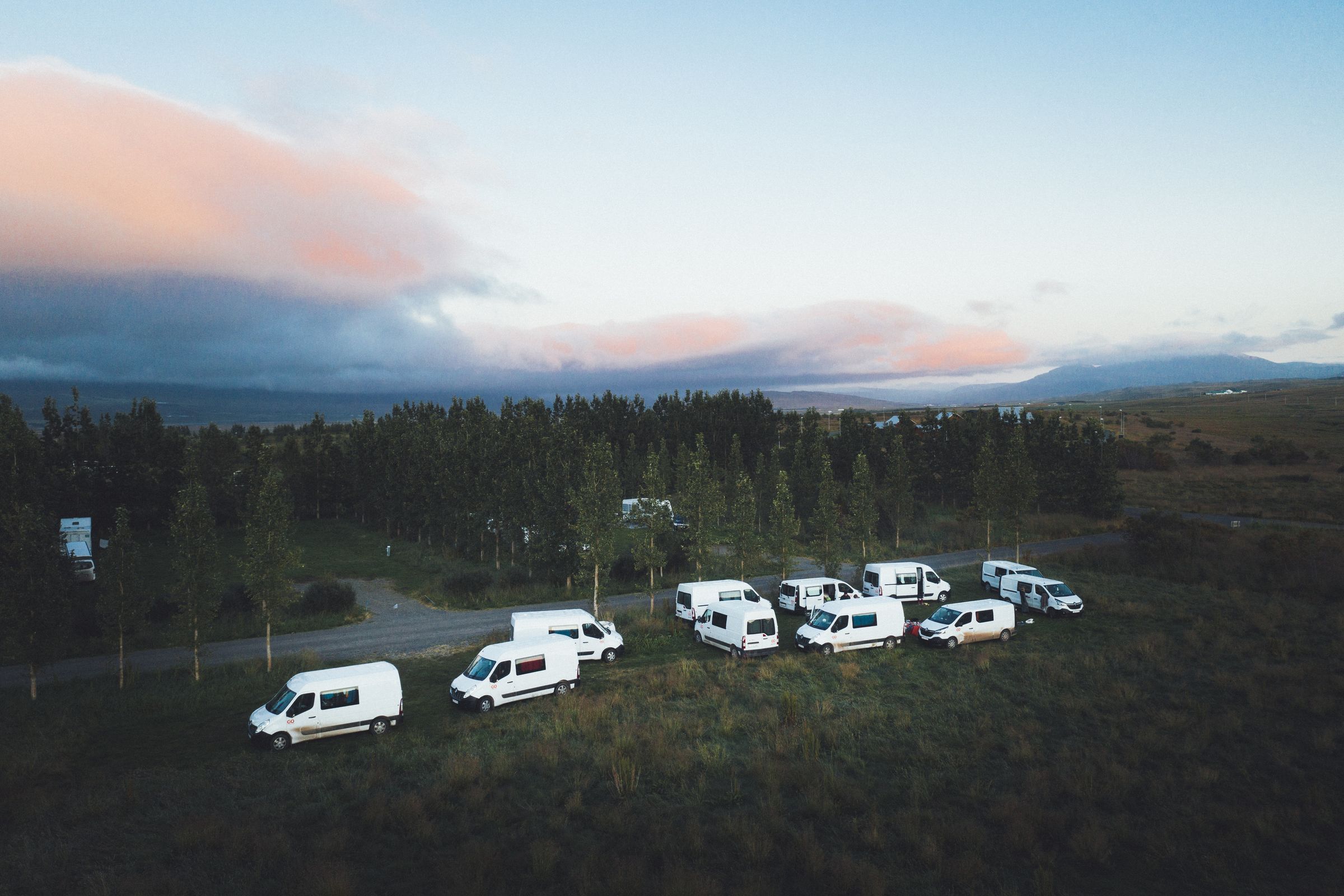an aerial view of a row of white vans parked in a field .
