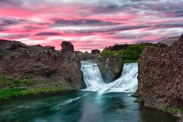 a waterfall is surrounded by rocks and a river at sunset at hjálparfoss in Iceland.