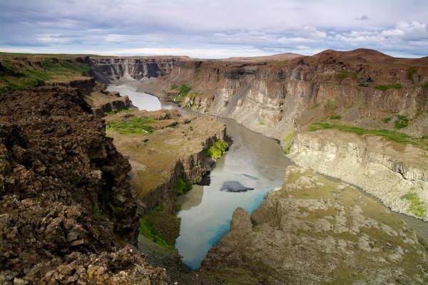 A rugged canyon with a glacial river winding between steep, rocky walls under a cloudy sky.