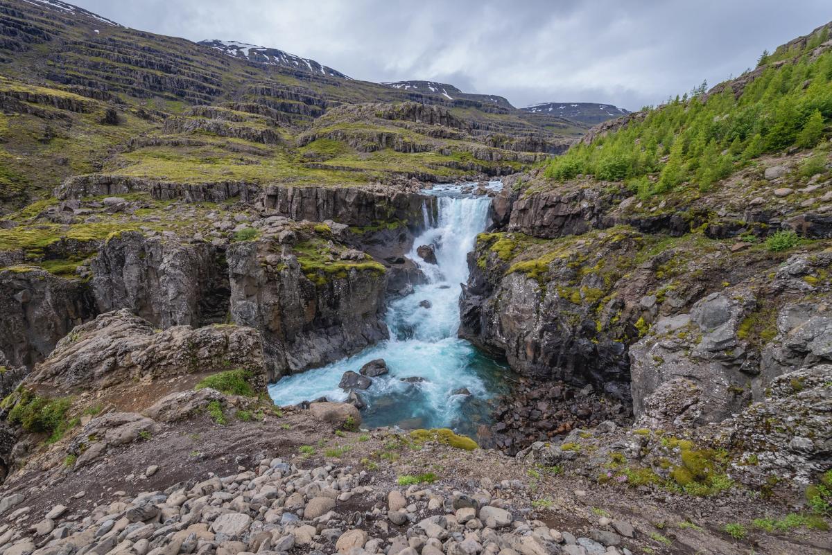 there is a waterfall in the middle of a canyon in the mountains in east iceland.