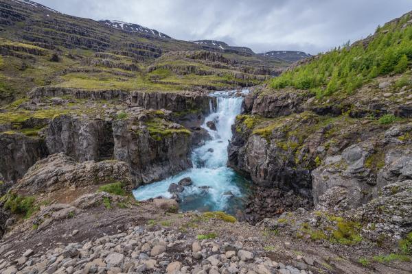 there is a waterfall in the middle of a canyon in the mountains in east iceland.