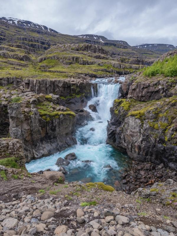 there is a waterfall in the middle of a canyon in the mountains in east iceland.