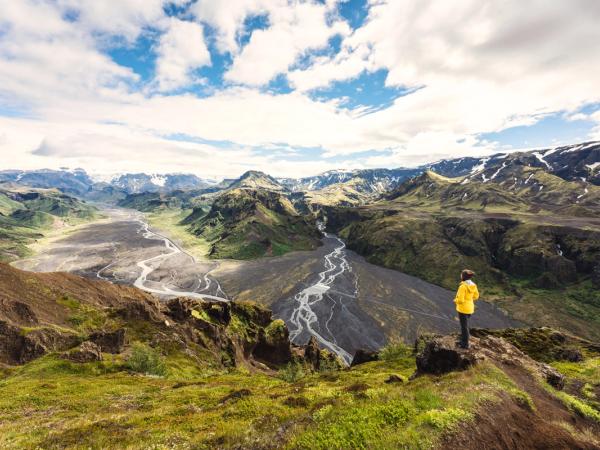 a man in a yellow jacket is standing on top of a mountain overlooking a river .