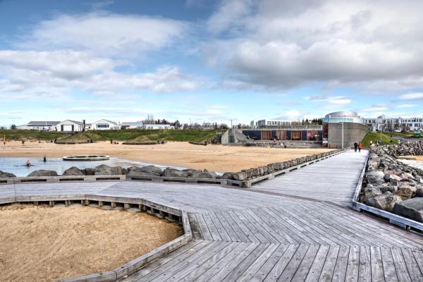 Wooden boardwalk leading to a sandy beach with people and modern buildings.