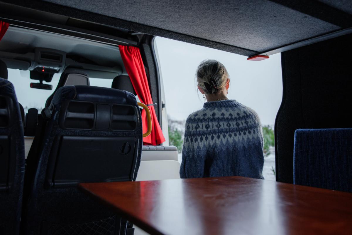 Frau sitzt neben dem Tisch in der offenen Seitentür eines großen Wohnmobils für fünf Personen