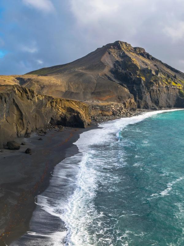 an aerial view of a black sandy beach with a mountain in the background .