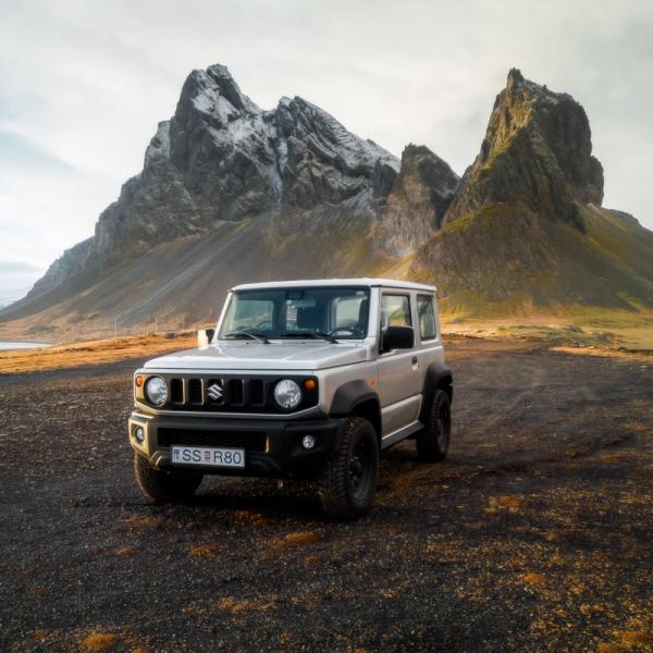 a white suzuki jimny is parked in front of a mountain .