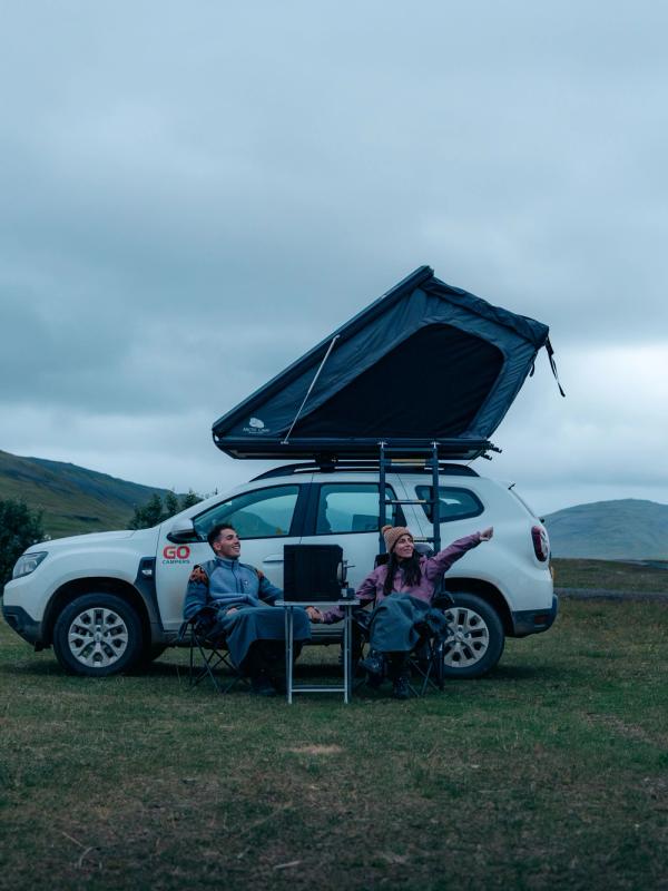 Una pareja sentada en unas sillas fuera de un coche con una tienda de campaña en el techo