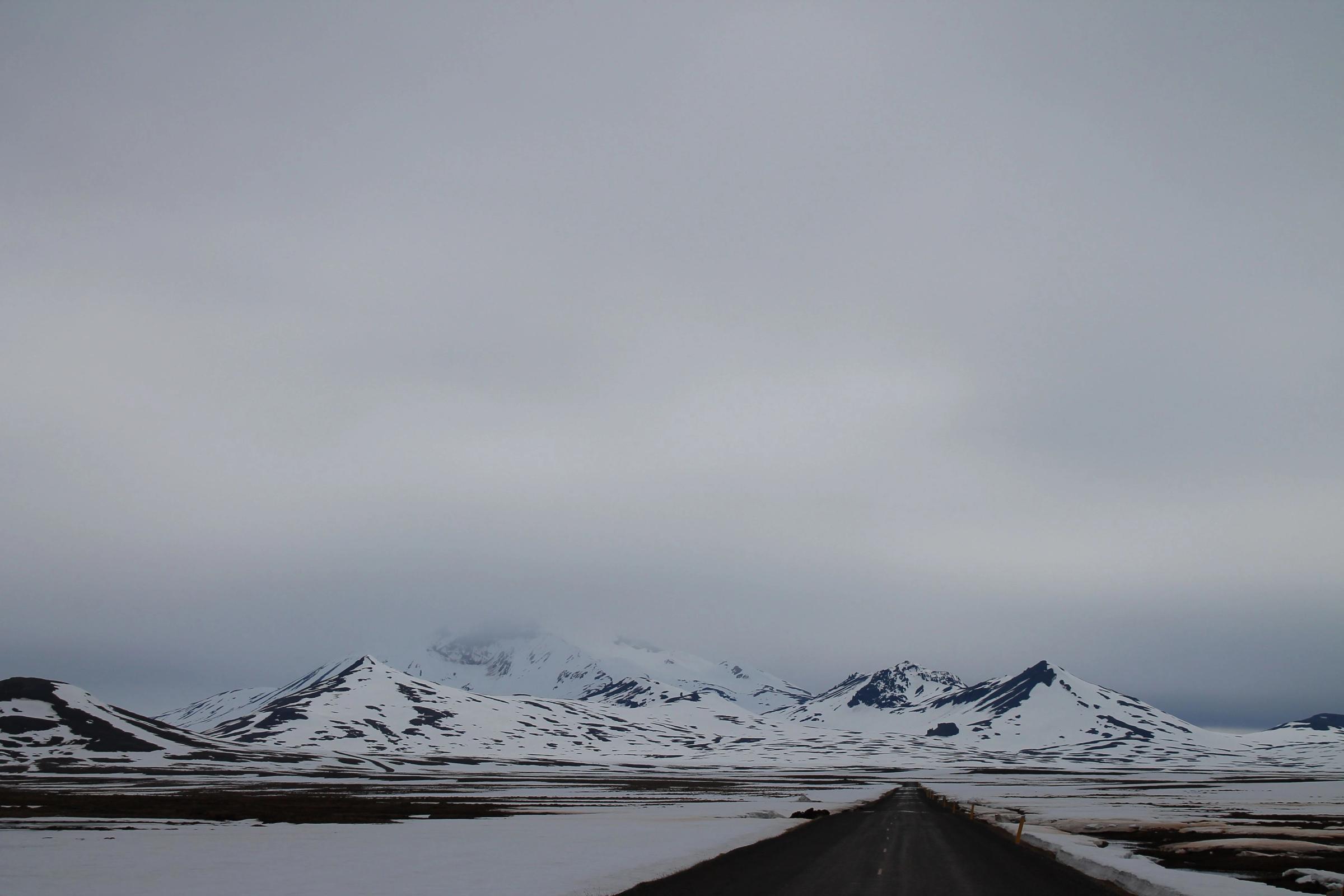 a road going through a snowy landscape with mountains in the background .