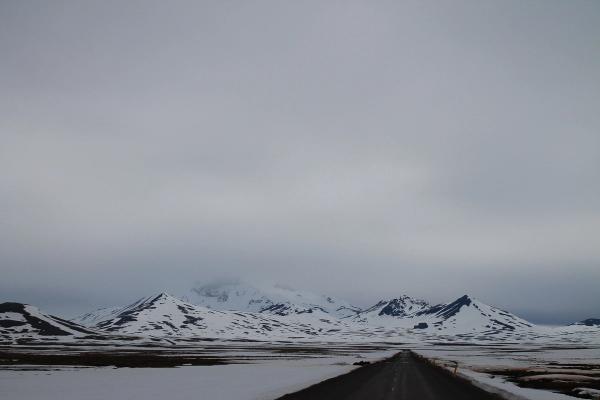 a road going through a snowy landscape with mountains in the background .