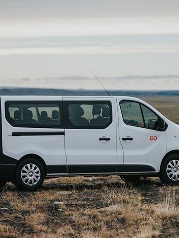 a woman in a sweater stands in front of two cars