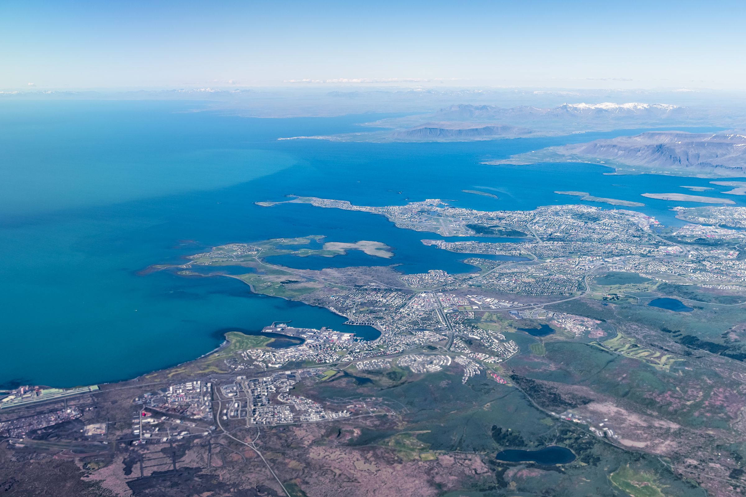 an aerial view of a city surrounded by water and mountains in an airplane above Iceland.