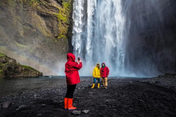 a woman taking a picture of two people in front of a waterfall