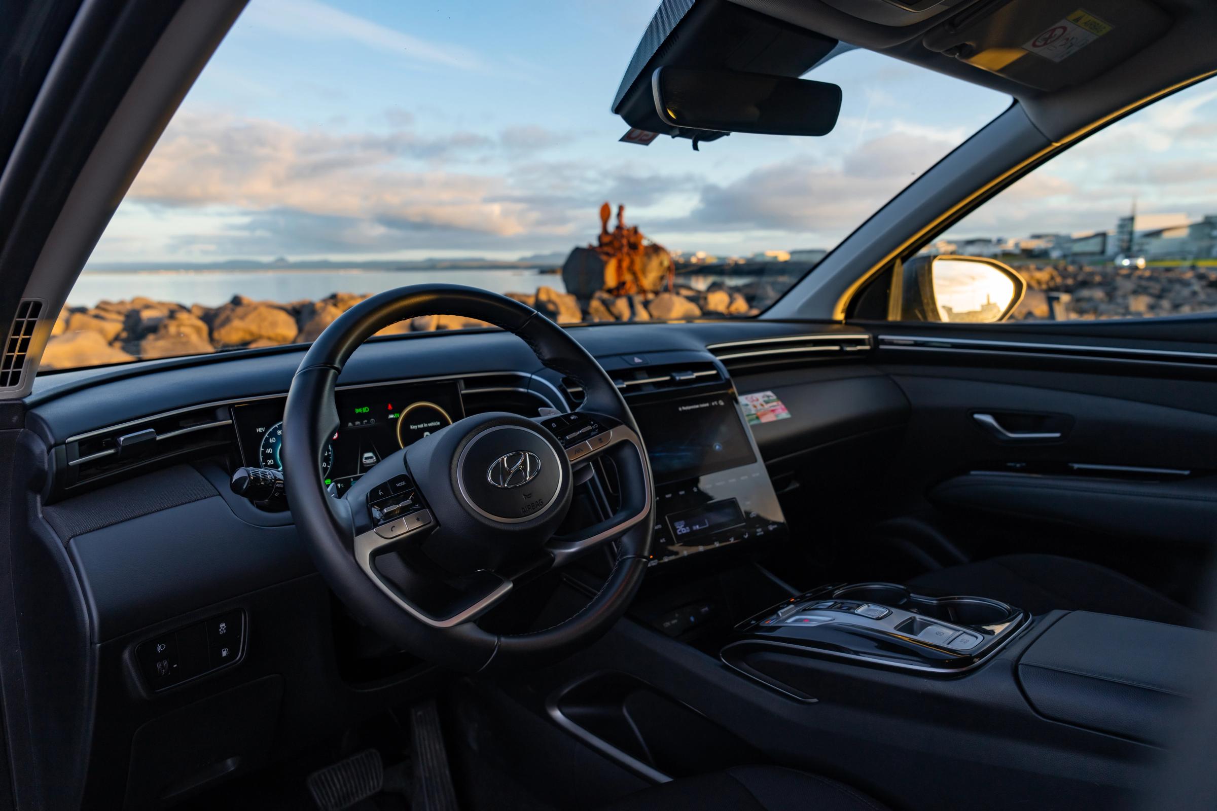 Tableau de bord d’un Hyundai Tucson avec volant, écran numérique conducteur et écran tactile central, face à une côte rocheuse