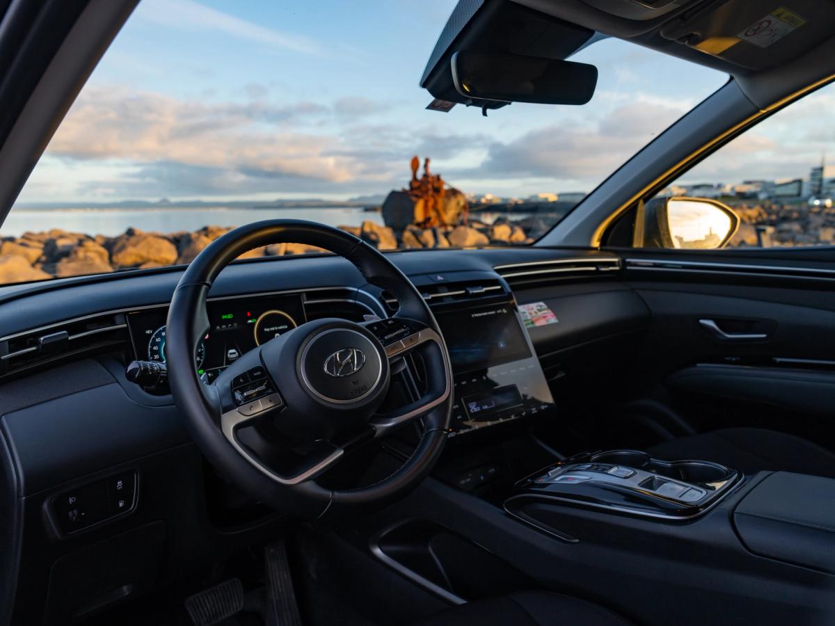 Intérieur du tableau de bord du Tucson Tableau de bord d’un Hyundai Tucson avec volant, écran numérique conducteur et écran tactile central, face à une côte rocheuse