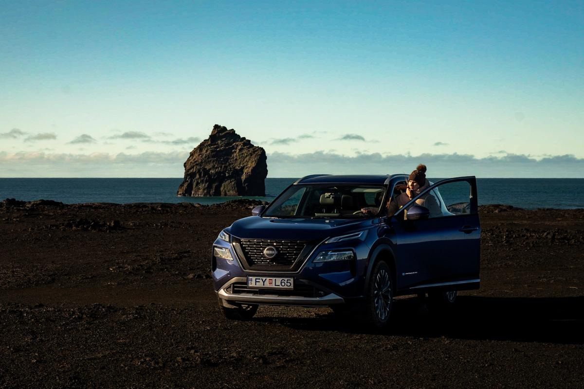 SUV Nissan X-Trail estacionado con la puerta abierta junto a una formación rocosa costera