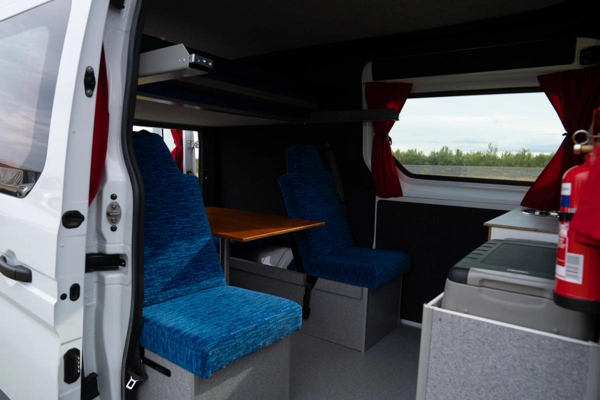 Dining area with facing blue seats around a wooden table, cool box and fire extinguisher