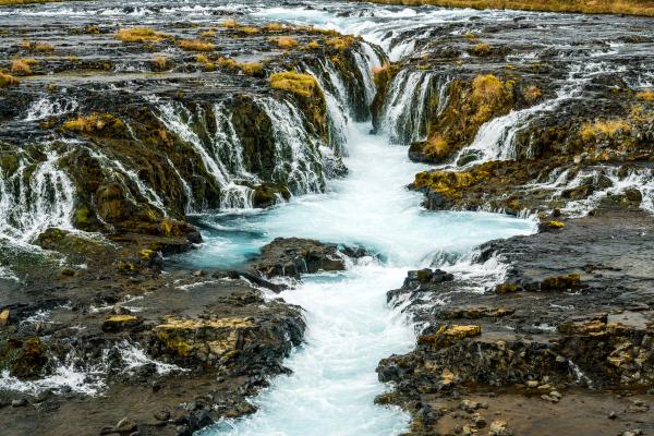 a waterfall is surrounded by rocks in the middle of a river at Brúarfoss in Iceland.