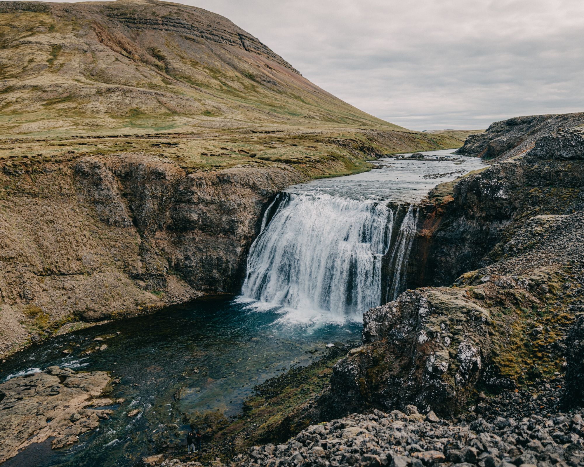 une cascade au milieu d'une montagne entourée de rochers et d'herbe.