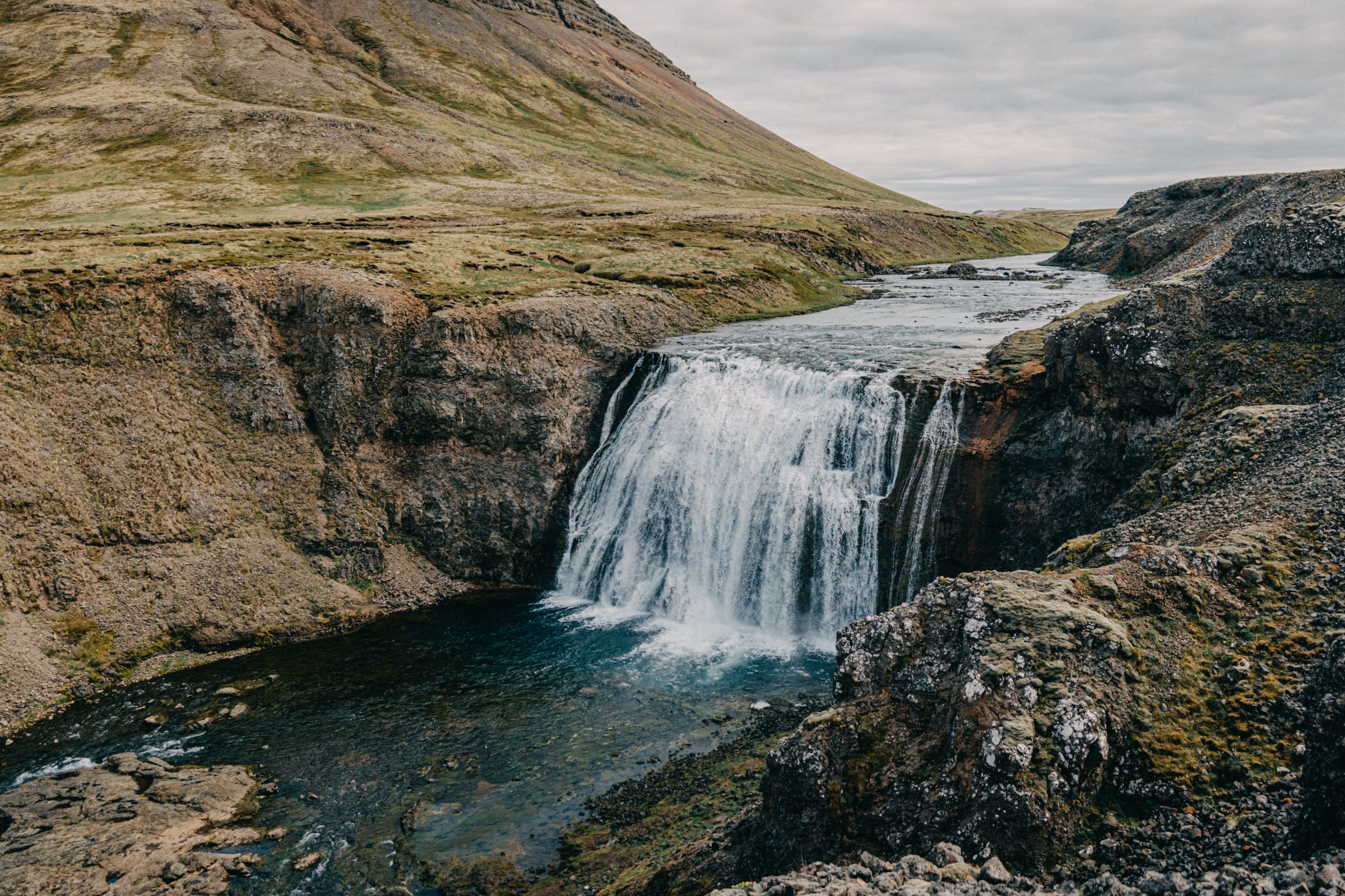 une cascade au milieu d'une montagne entourée de rochers et d'herbe.