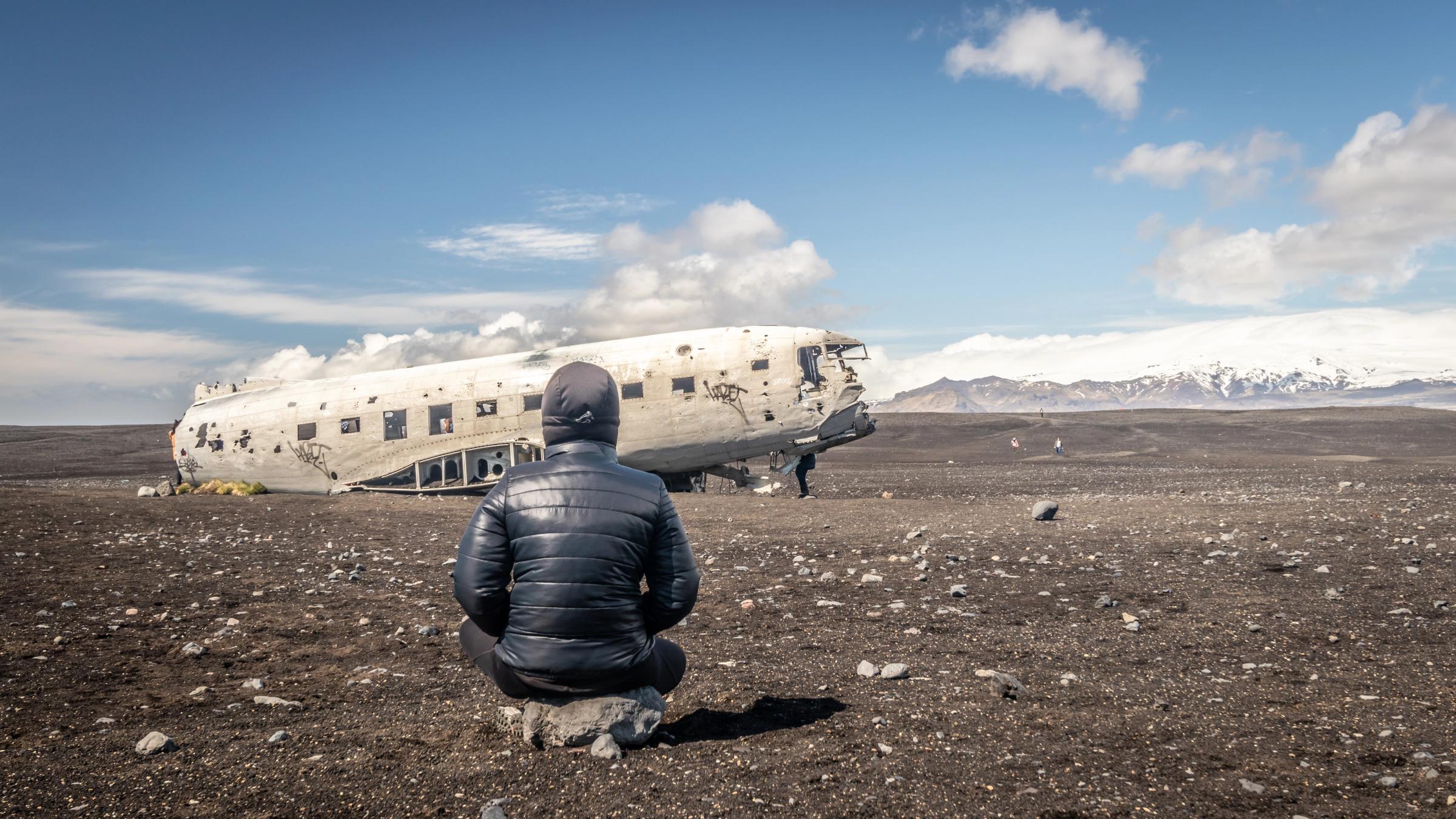 a man is kneeling in front of a wrecked airplane in the middle of a desert .
