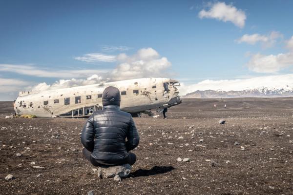 a person sitting on a black sand beach looking at a plane wreck