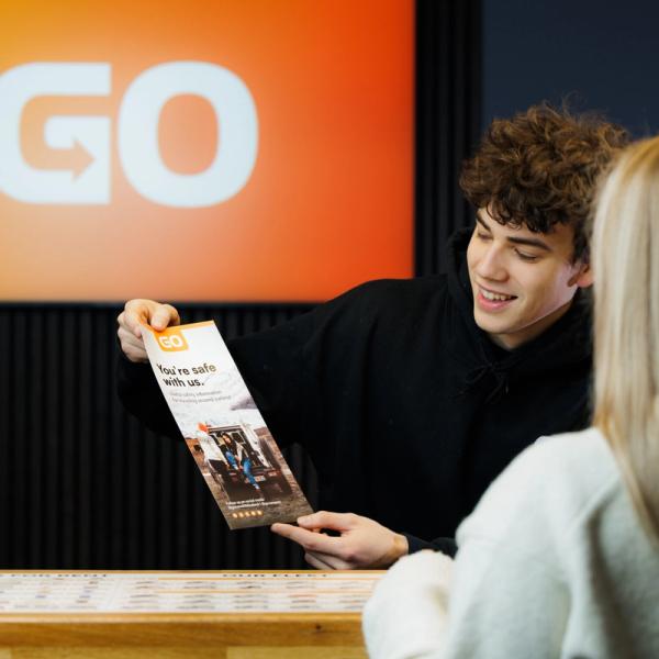 Un hombre entrega un folleto a una mujer en un mostrador.