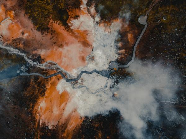 Aerial view of a geothermal landscape with vibrant colors, steam, and a winding path.