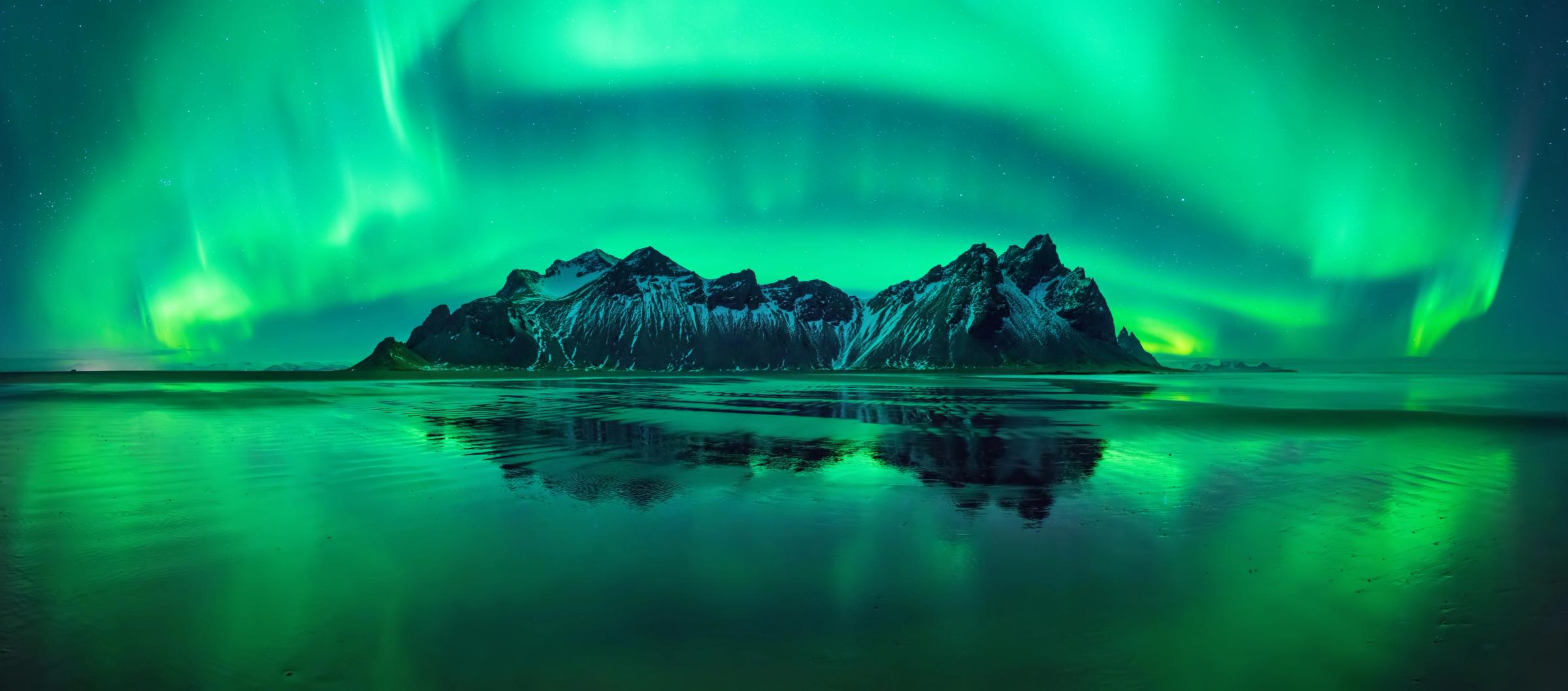 the aurora borealis is reflected in the water over the mountains .