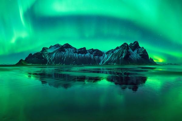 Aurora boreal reflajada en el agua y unas montañas